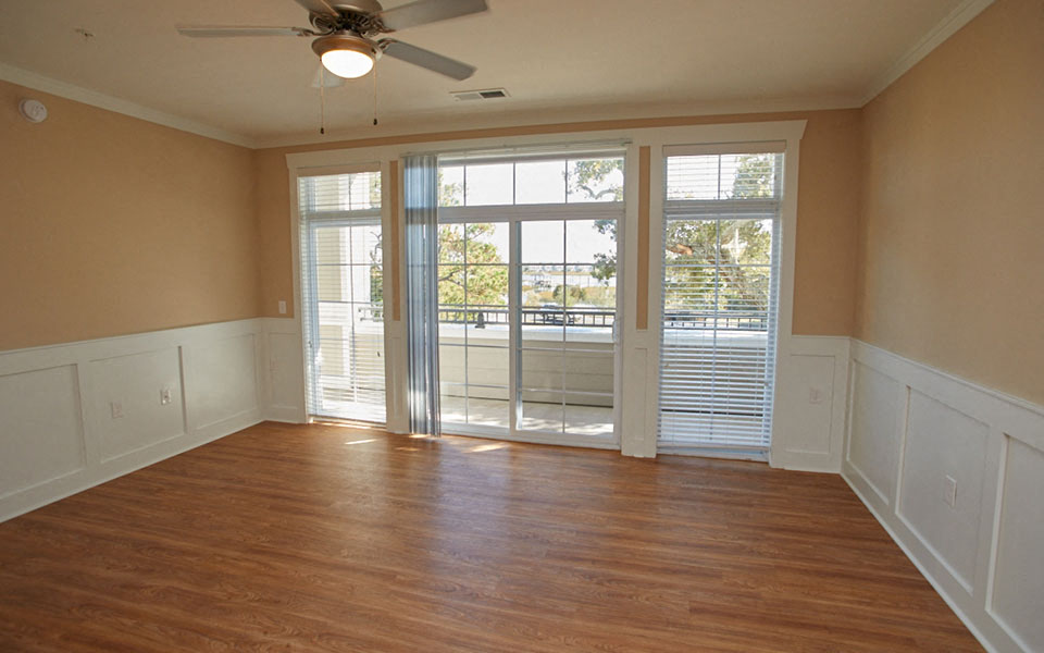 an empty living room with a ceiling fan and a balcony