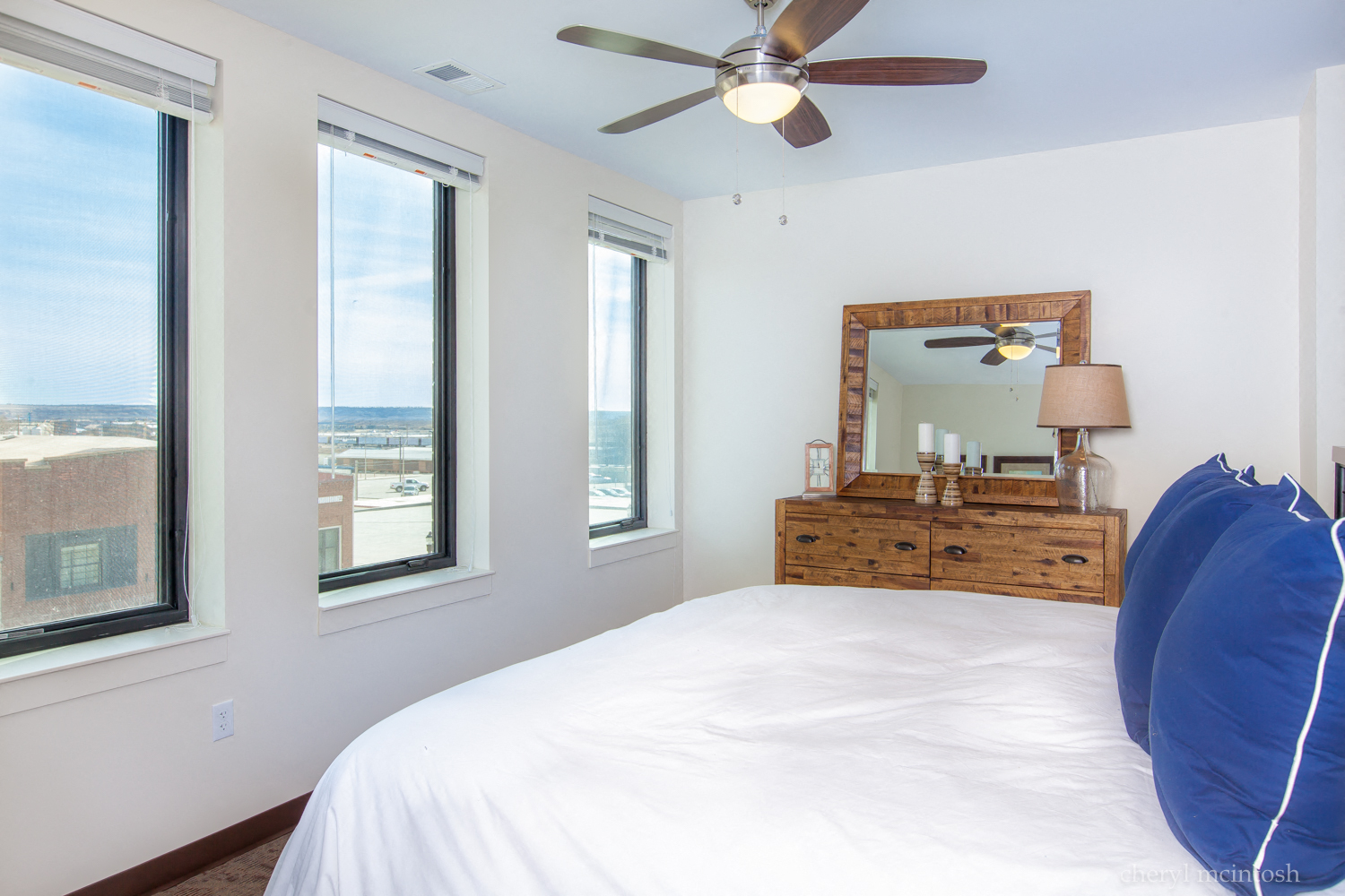 a bedroom with a white bed and a ceiling fan and three windows