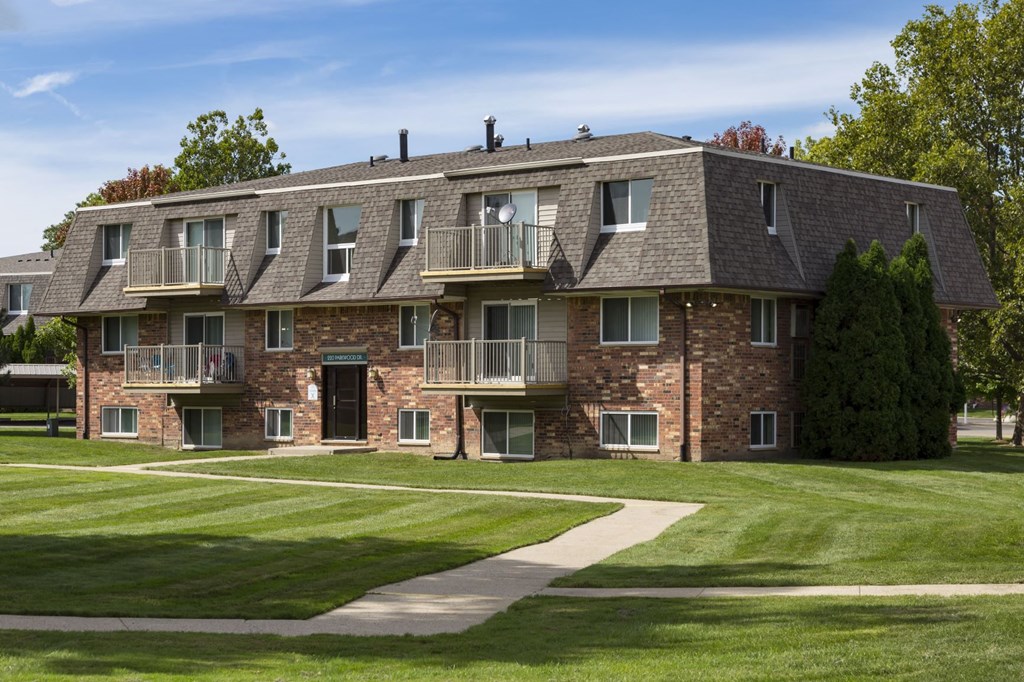 a large brick apartment building with a lawn and sidewalk