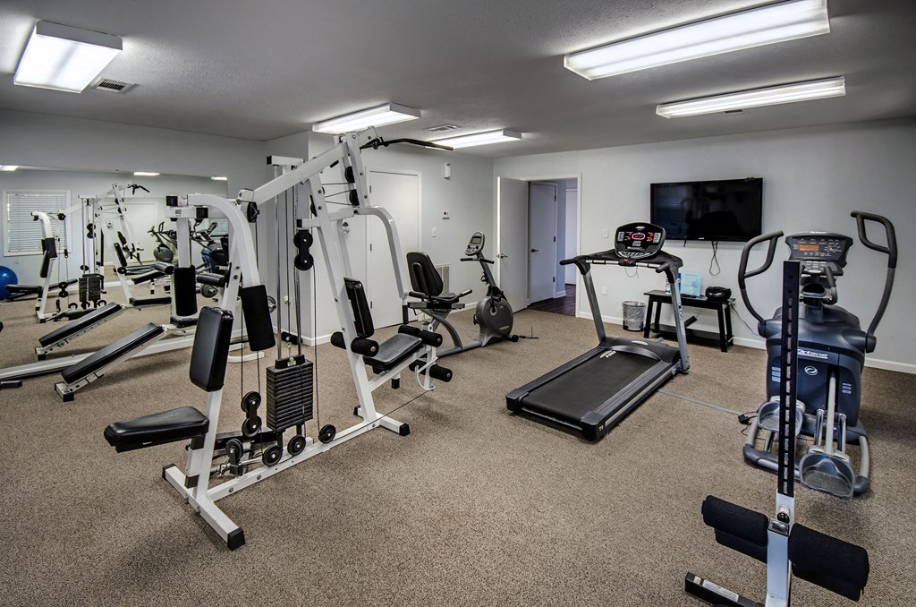 a gym with cardio equipment and weights on the floor and a tv