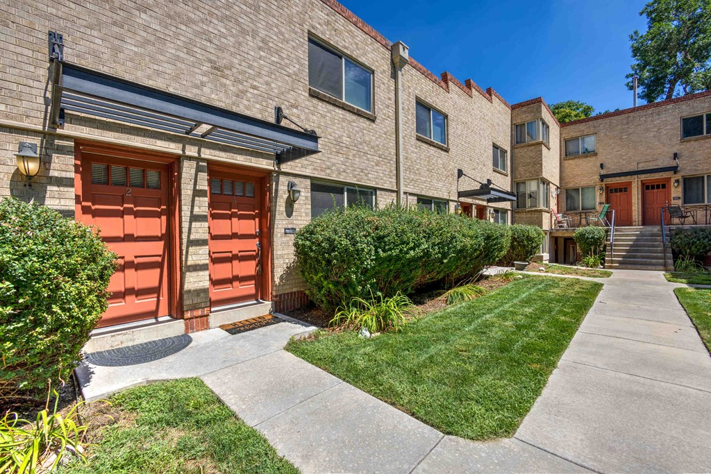 a sidewalk in front of a brick apartment building with red doors