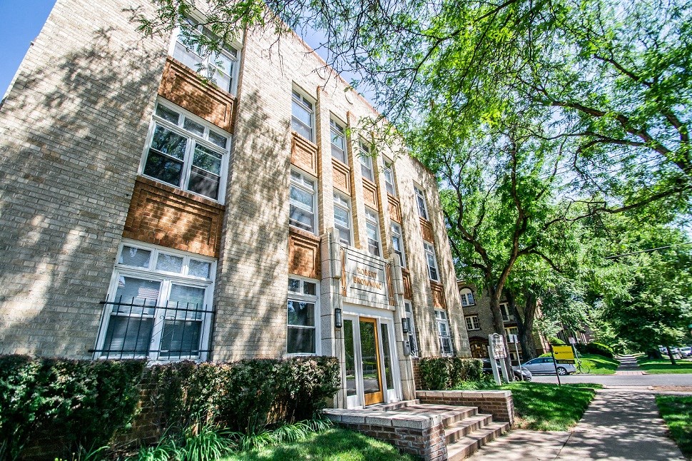 a large brick apartment building with trees and a sidewalk