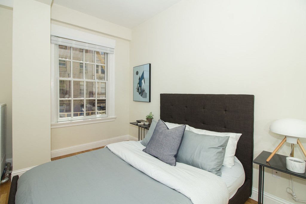 A bedroom with a bed, nightstand, and a window.