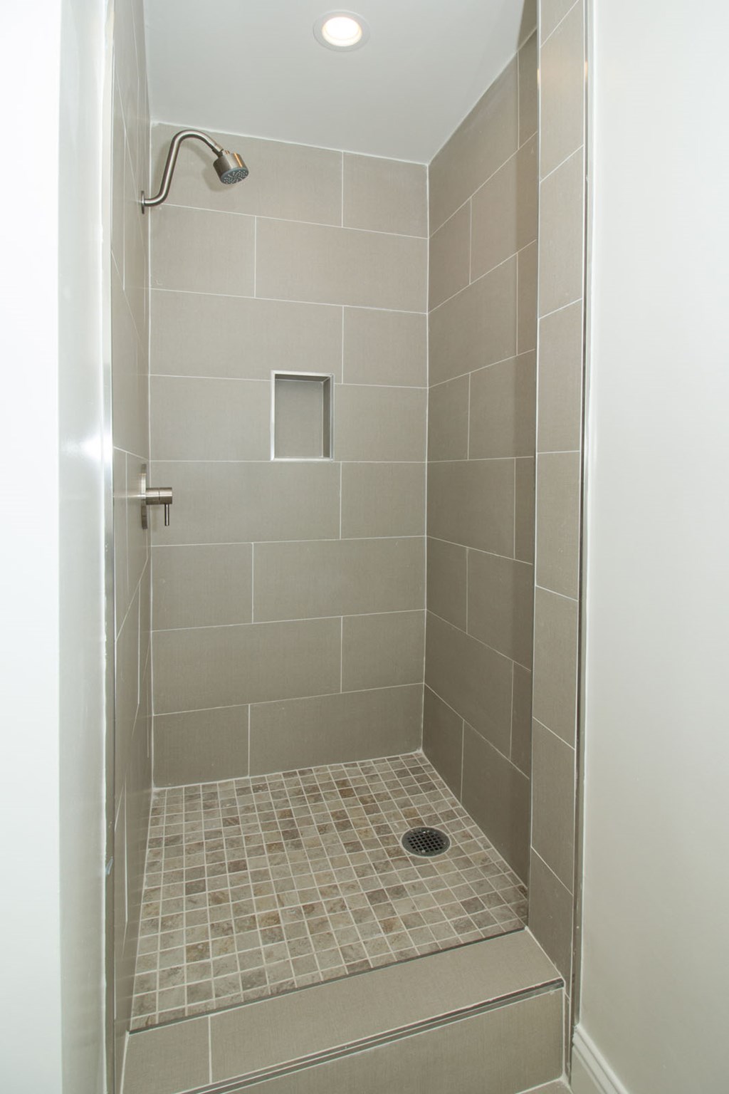 A shower with a drain in the middle of a tiled floor.