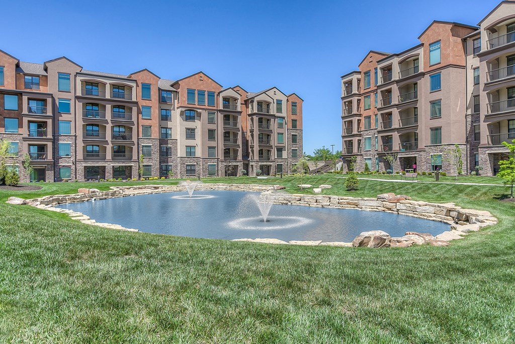 a fountain in the middle of a grassy area with an apartment complex in the background  at EdgeWater at City Center, Lenexa, 66219