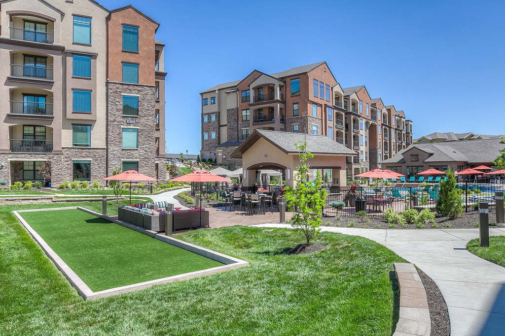 a grassy area with umbrellas and tables and chairs in front of an apartment building at EdgeWater at City Center, Lenexa, Kansas