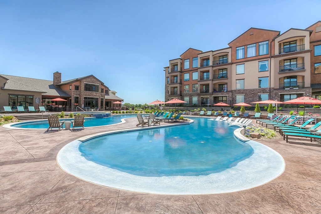a swimming pool with lounge chairs and umbrellas with a resort style building in the background at EdgeWater at City Center, Lenexa