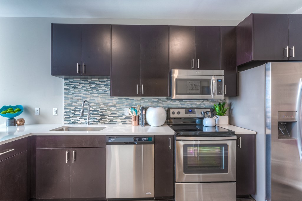 a kitchen with dark cabinets and stainless steel appliances  at EdgeWater at City Center, Lenexa, KS