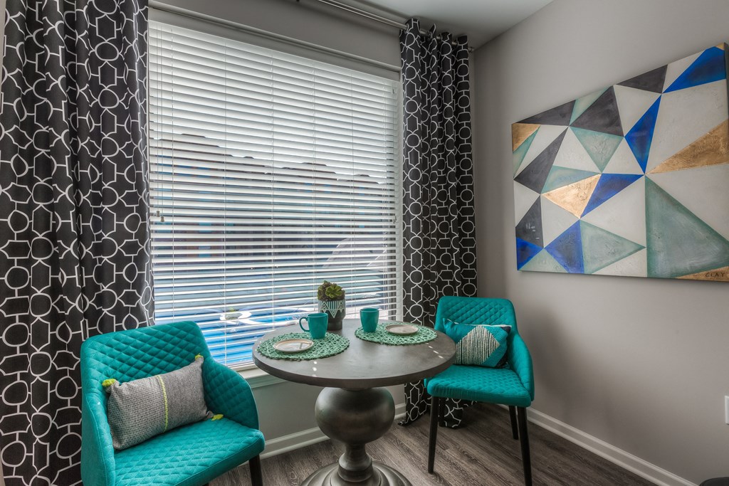 a small dining table with two blue chairs and a large window with blinds a small dining table with two blue chairs and a large window with blinds at EdgeWater at City Center, Lenexa, KS