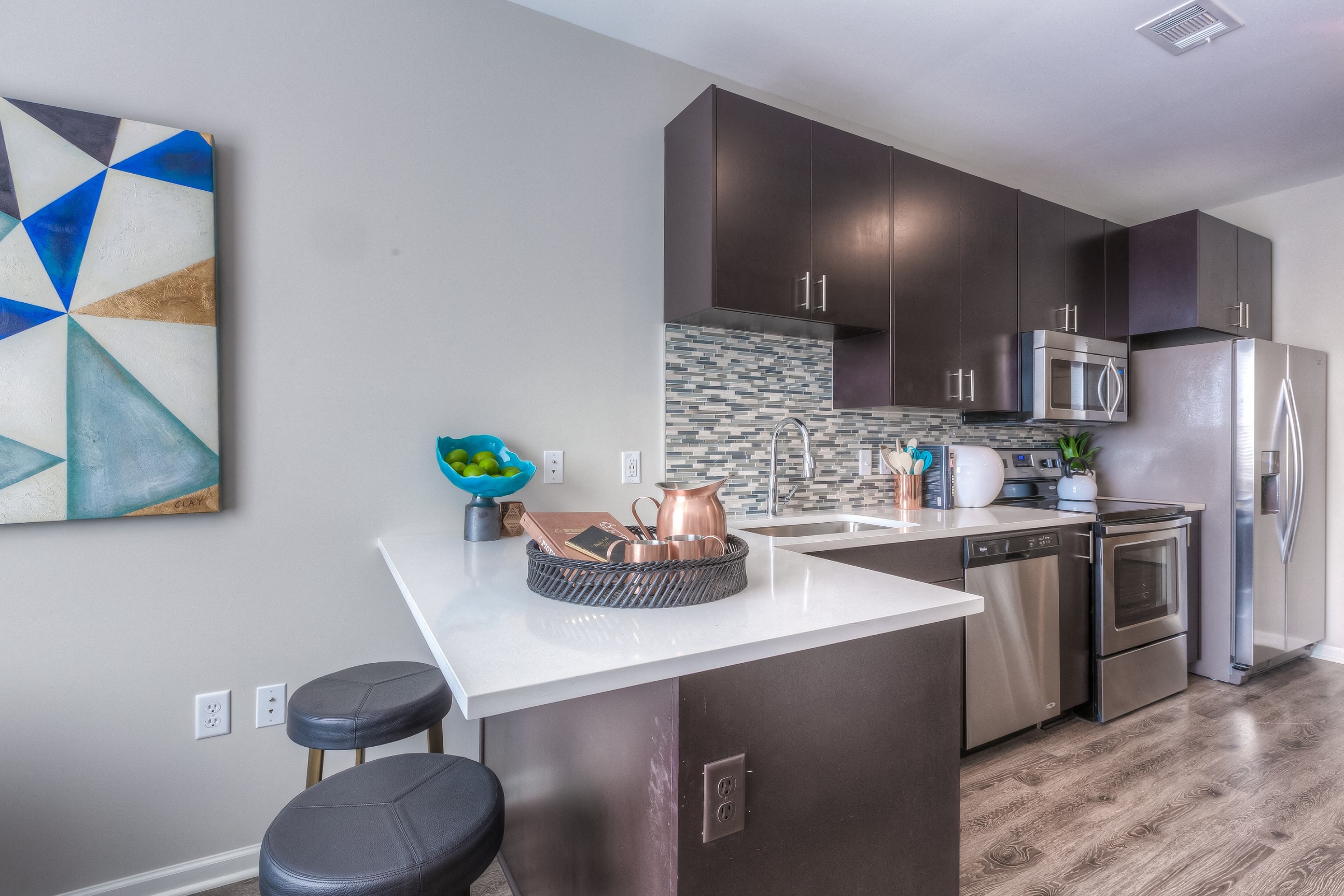 a kitchen with dark cabinets and a white counter top with two stools in front of it  at EdgeWater at City Center, Lenexa