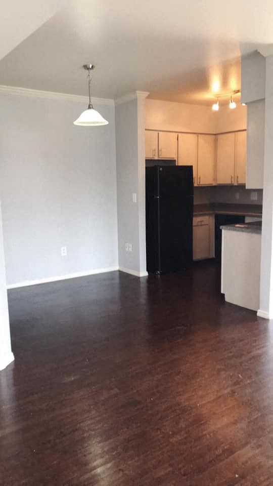 an empty living room with wood floors and a black refrigerator