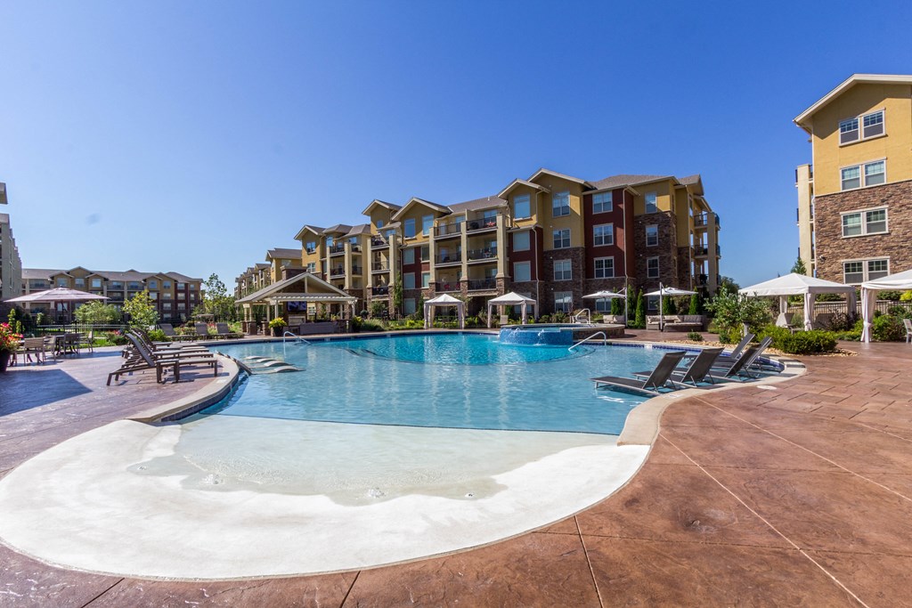 a swimming pool with lounge chairs and umbrellas with an apartment building in the background  at WaterCrest at City Center, Lenexa, Kansas