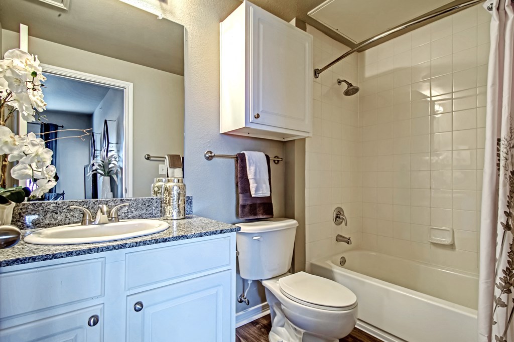 bathroom in one bedroom floorplan with white cabinets and granite countertops