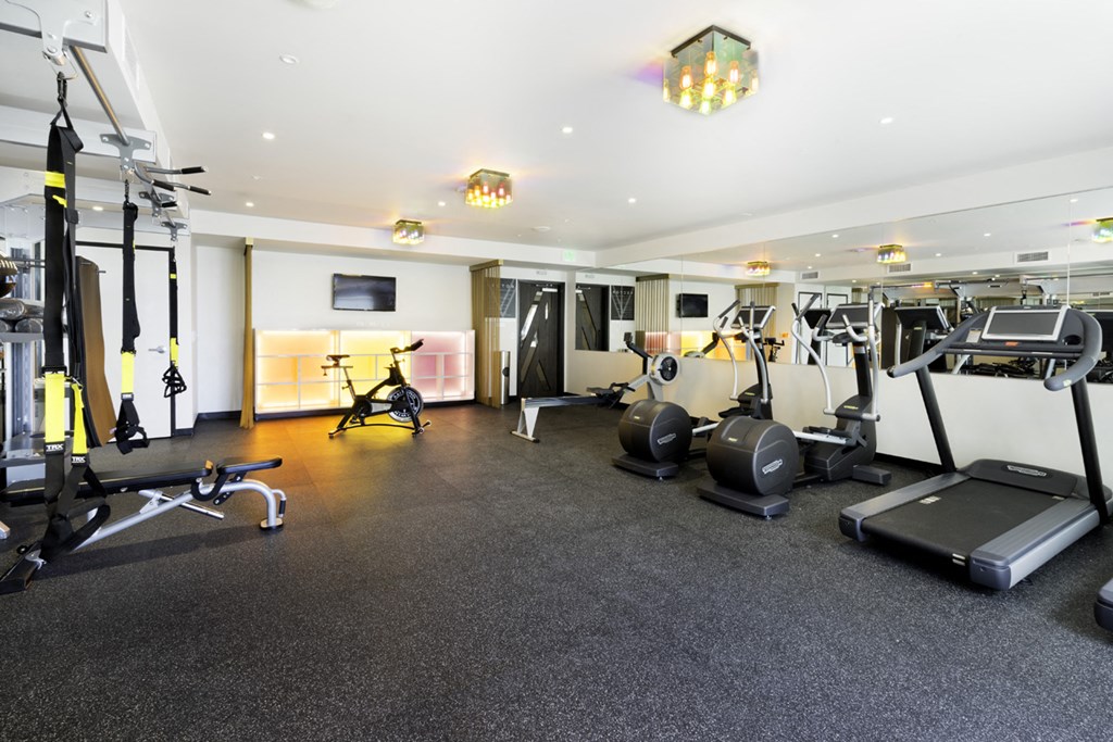 a gym with weights and cardio equipment on the floor and a tv
