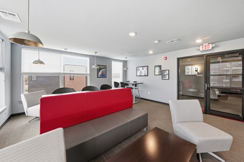 A modern office space with a red and grey couch, a wooden table, and a glass door leading to another room.