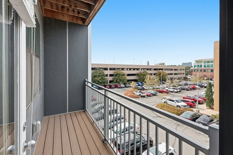 A balcony with a wooden floor overlooks a parking lot.