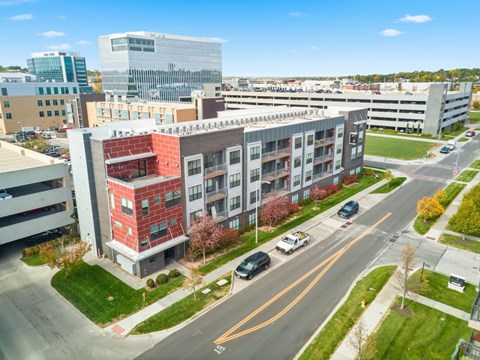 A red brick building is in the middle of a road with cars driving by.