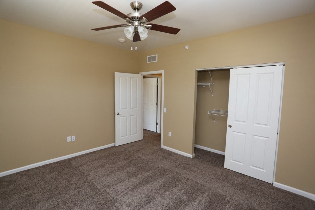 an empty living room with a ceiling fan and a closet