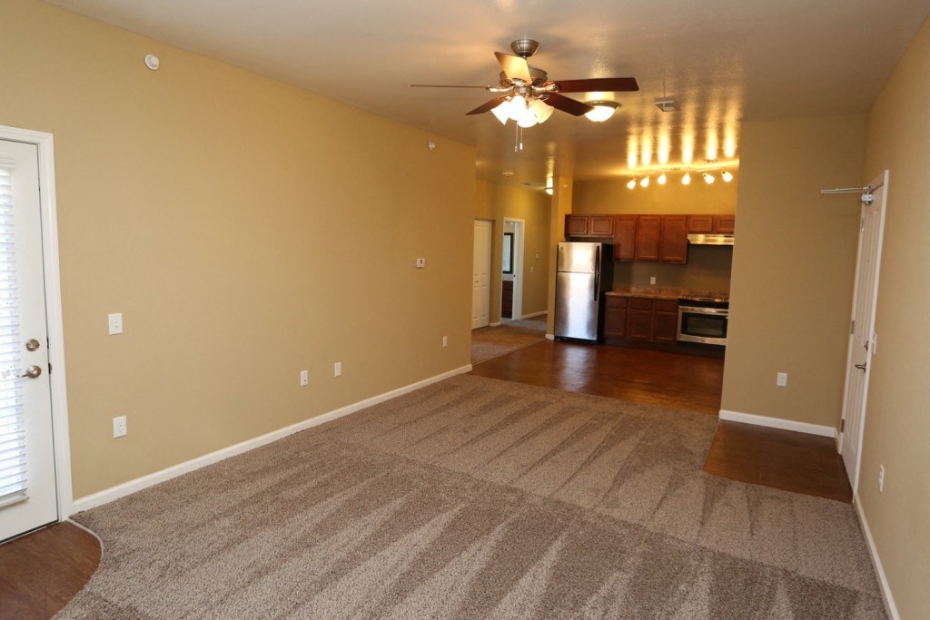 a empty living room with a ceiling fan and a kitchen