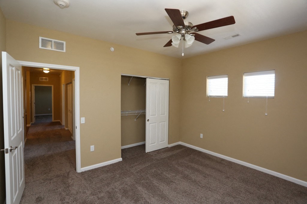 an empty living room with a ceiling fan and a closet