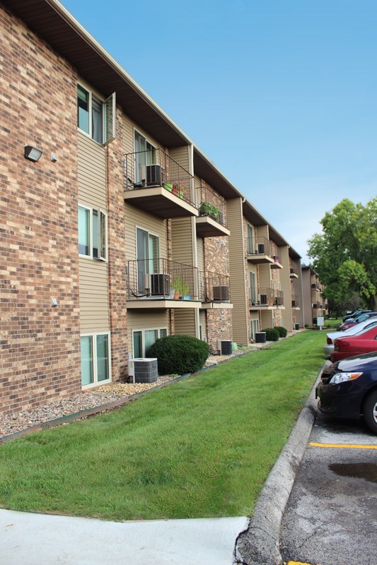 an apartment building with a lawn and cars parked in front