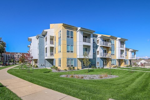 an exterior view of an apartment building with green grass and a sidewalk