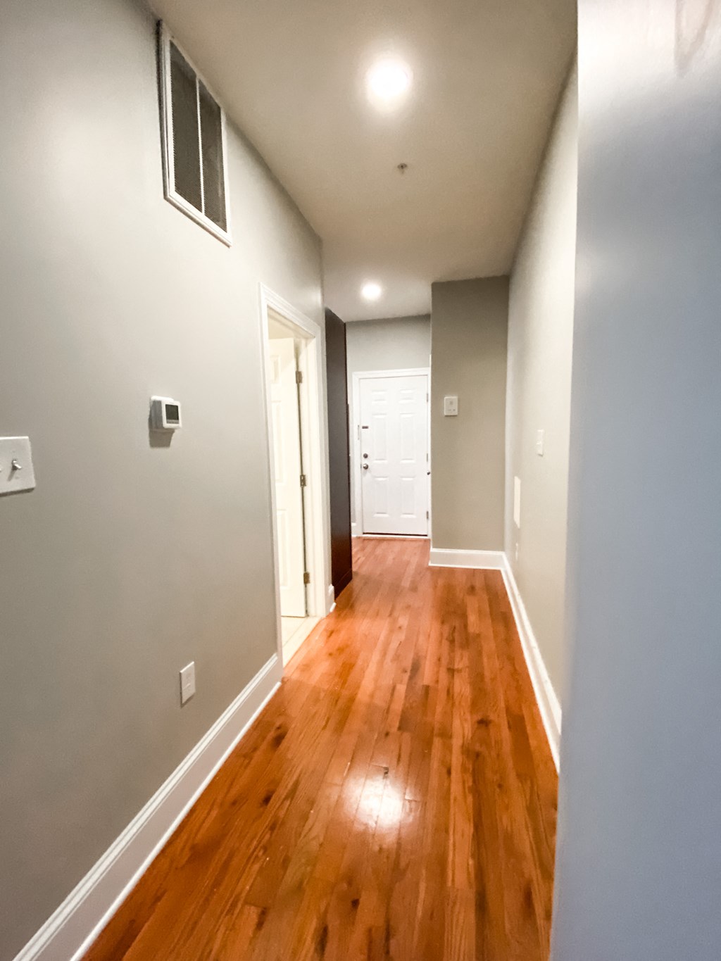 a hallway with wood floors and grey walls and a door to a closet