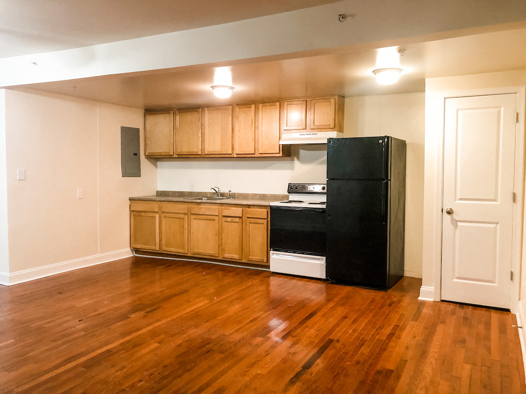 an empty kitchen with wood flooring and a black refrigerator