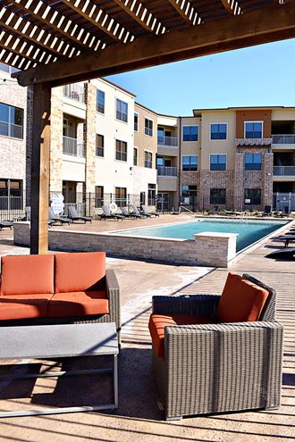 a patio with chairs and a pool in front of an apartment building