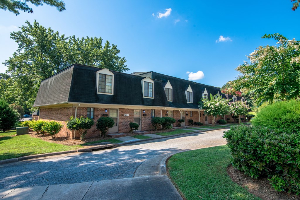 the front of a brick house with a driveway and trees