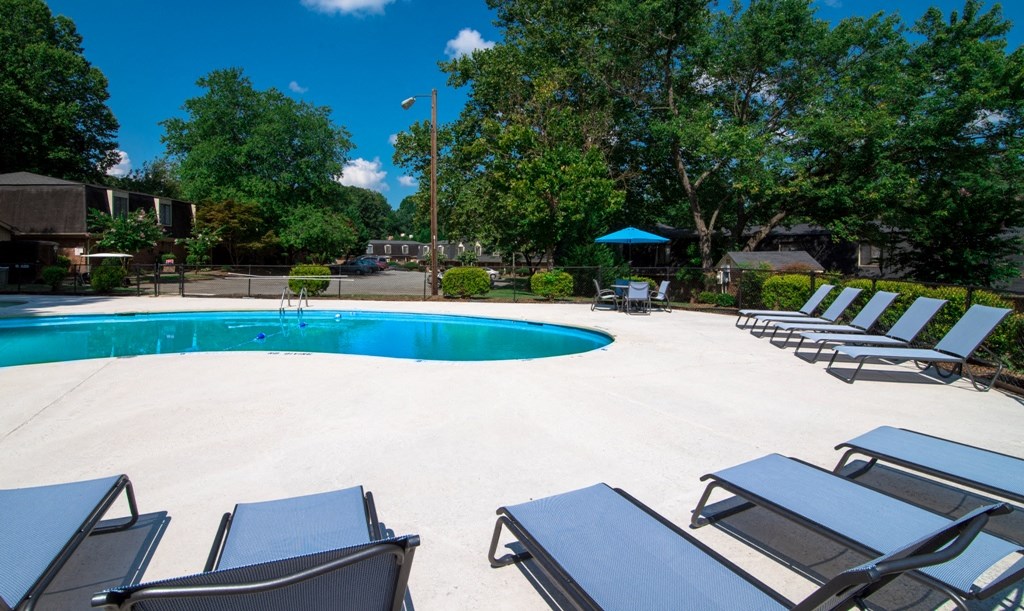 a swimming pool with chairs around it and trees in the background