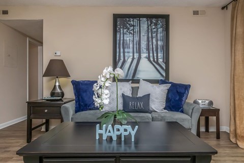 A living room with a grey couch and a coffee table with the word "HAPPY" on it.