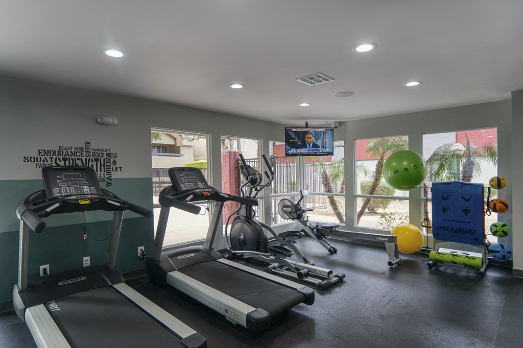 a gym with treadmills and other exercise equipment in a room with windows