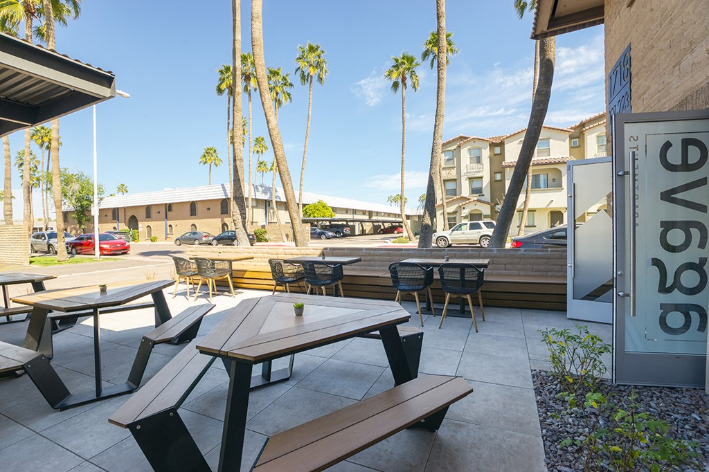 a patio with tables and chairs outside of a restaurant with palm trees