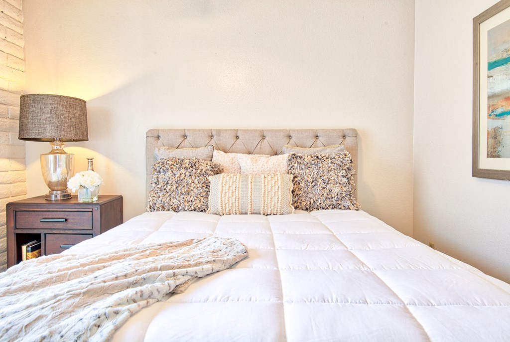 a bedroom with a bed with pillows and a nightstand with a lamp