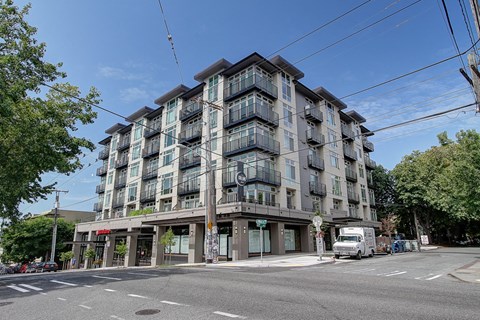 A large apartment building with balconies and a red awning is situated on a street corner.
