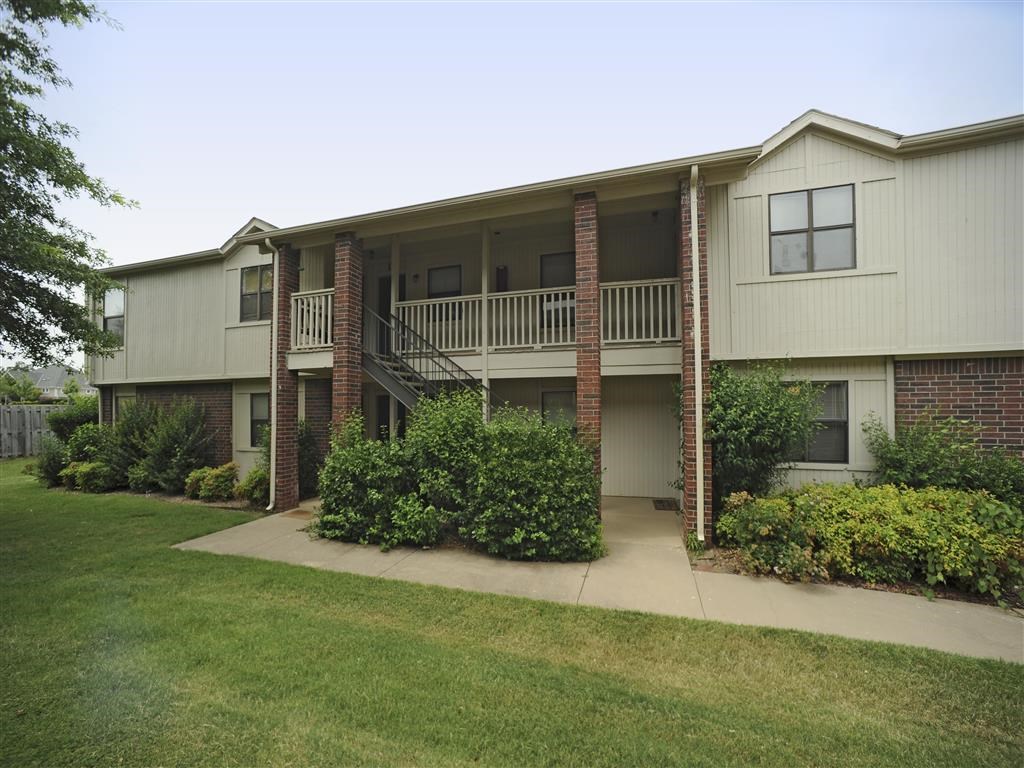 an exterior view of an apartment building with a yard and a balcony