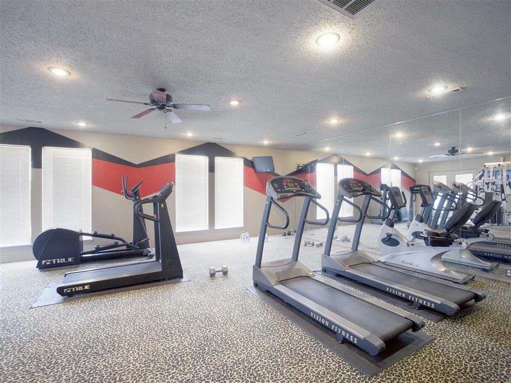 a gym with cardio machines and a ceiling fan