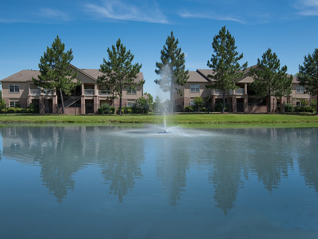 a fountain in the middle of a pond in front of apartment buildings