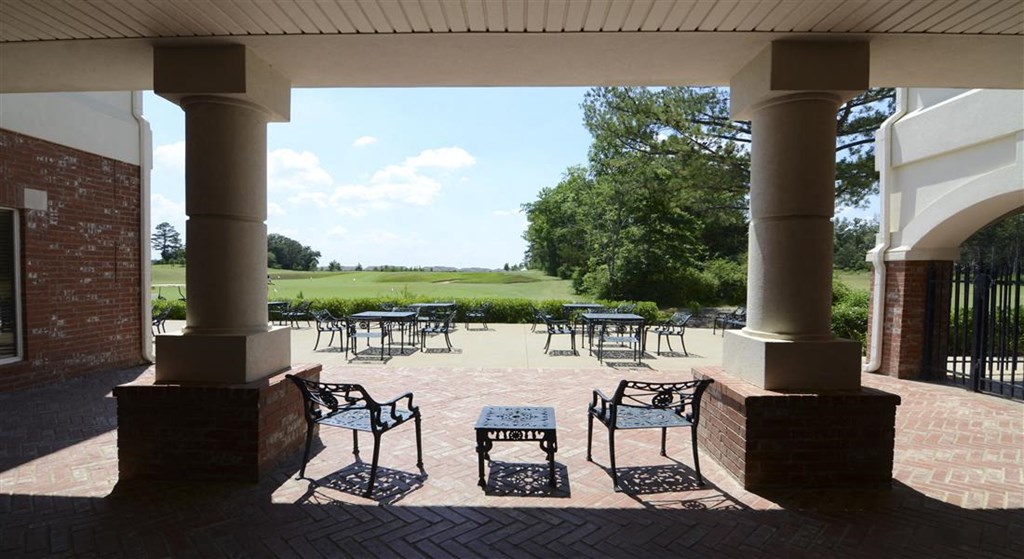 a patio with tables and chairs and a golf course in the background