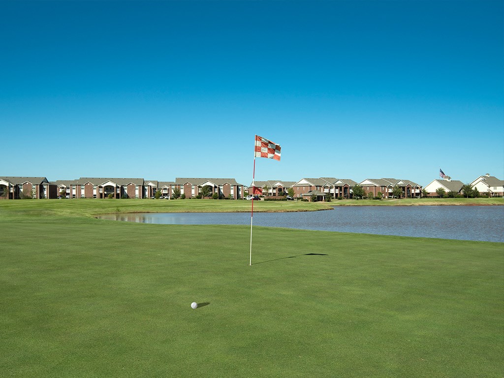 a flag on a golf course next to a pond with houses in the background