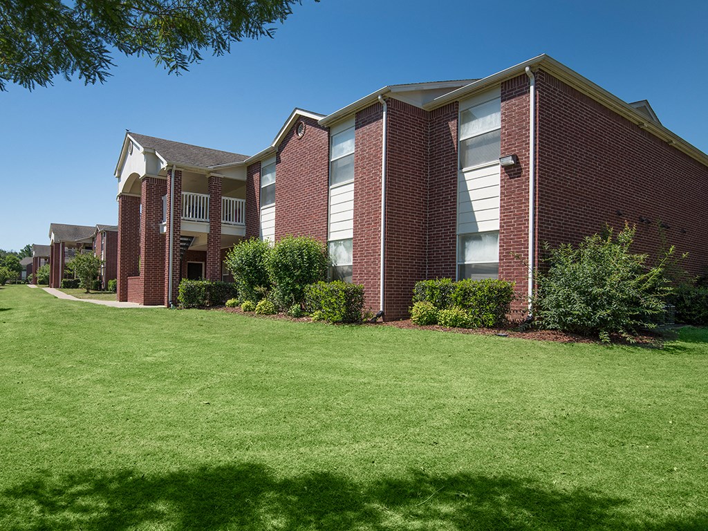 a brick building with green grass and bushes in front of it