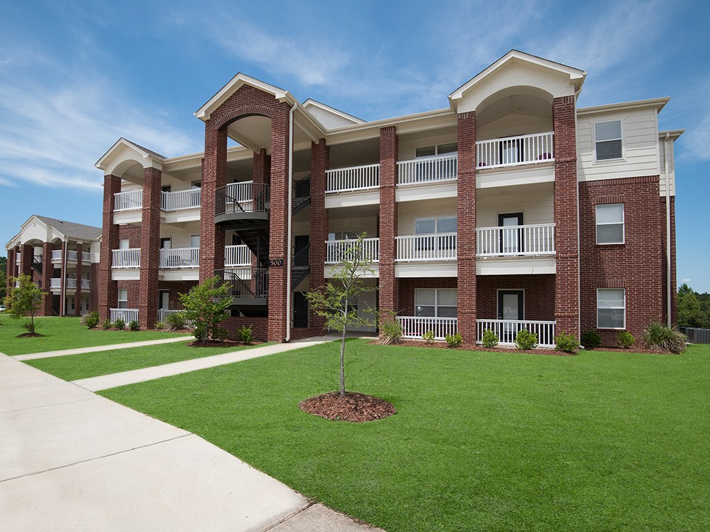 an exterior view of an apartment building with green grass and a sidewalk