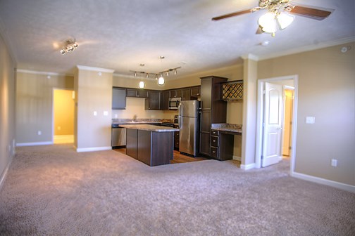 an empty living room with a kitchen and a ceiling fan