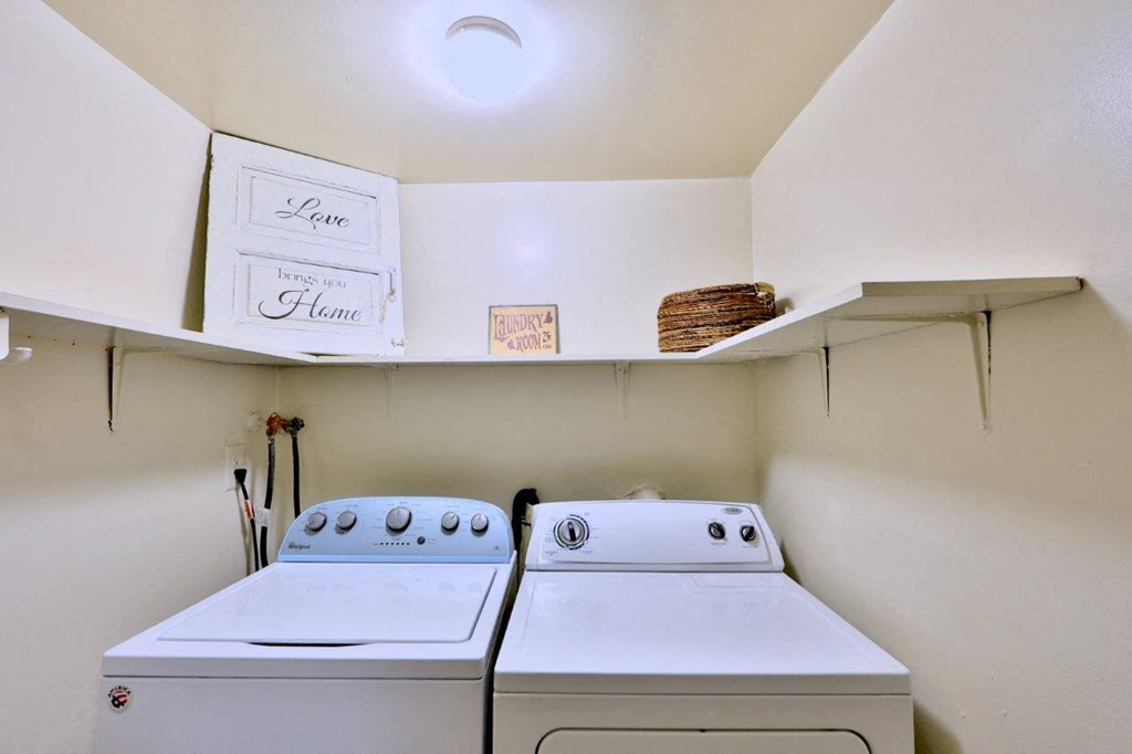 two washers and a dryer in a laundry room with a shelf above them