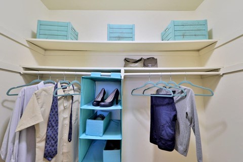 a walk in closet with blue shelves and clothes hanging