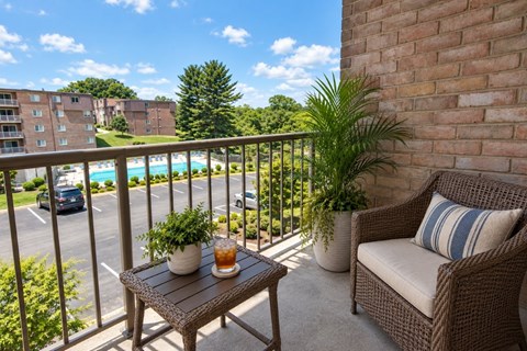 A balcony with a table, chairs, and a view of a pool and buildings.