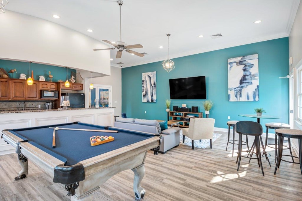 A pool table is in the middle of a room with a television and a bar area.