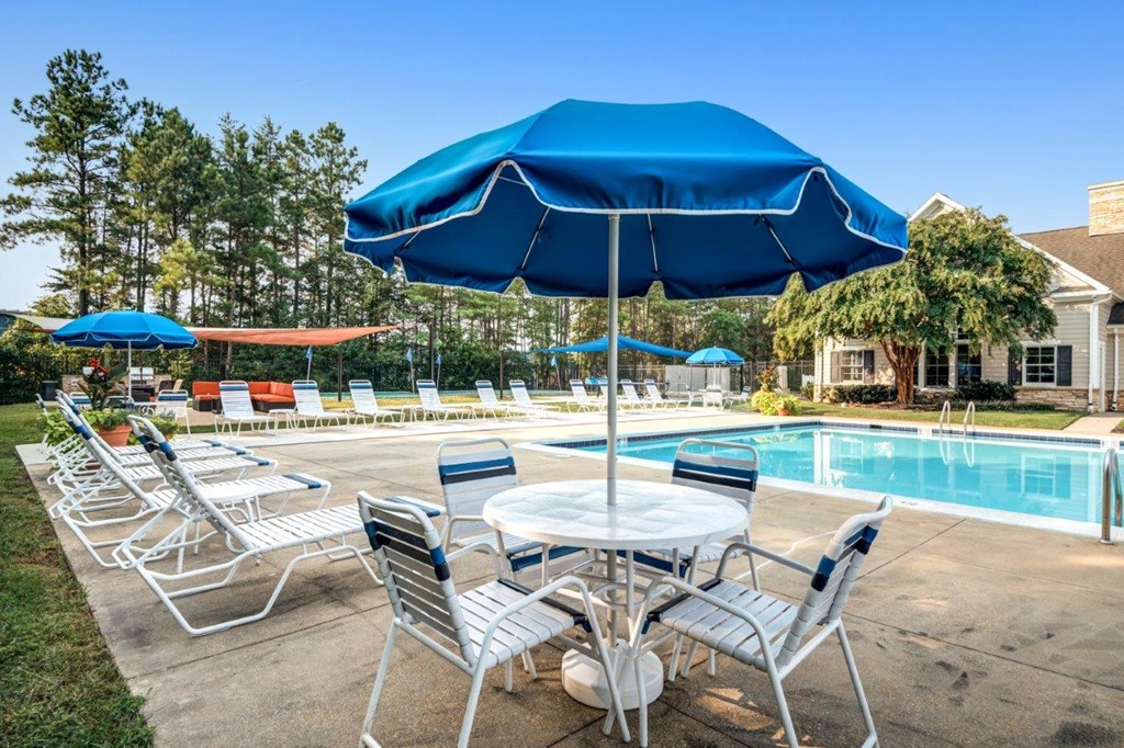 A blue umbrella shades a table under a pool.