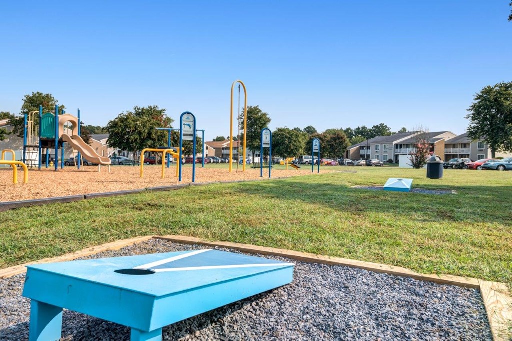 A blue table is in the middle of a gravel area with a playground in the background.